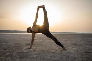 giovane donna in forma che allena le pose di yoga nel deserto durante il tramonto o l'alba, la donna in abbigliamento sportivo nero fa esercizi di stretching foto