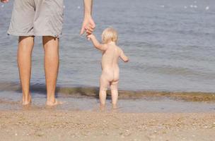 immagine ravvicinata di padre con un bambino di un anno che cammina sulla spiaggia in estate foto