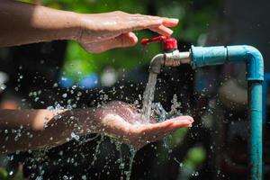 concetto di acqua nella vita di tutti i giorni. mani che sostengono l'acqua che scorre dal rubinetto. schizzi d'acqua dal rubinetto foto