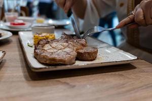 la vista parziale del primo piano della donna si diverte a mangiare la bistecca con forchetta e coltello nel ristorante foto