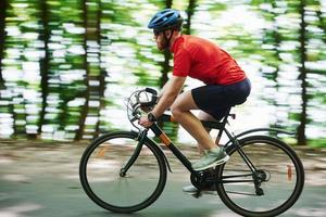 vento e aria fresca. il ciclista in bicicletta è sulla strada asfaltata nella foresta in una giornata di sole foto