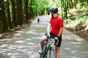 corridore dietro. il ciclista in bicicletta è sulla strada asfaltata nella foresta in una giornata di sole foto