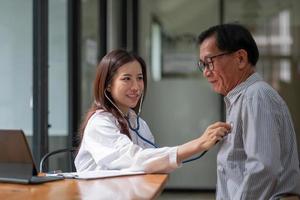 esame dello stetoscopio. medico femminile asiatico allegro attraente che ascolta gli anziani mentre usando lo stetoscopio foto