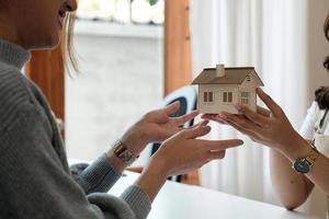 agente immobiliare o intermediario che fornisce un modello di casa con agente e cliente che discutono del contratto per l'acquisto, l'assicurazione o il prestito di immobili o proprietà foto