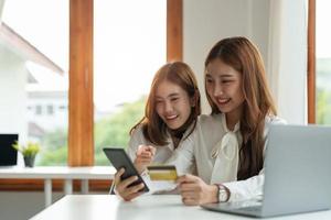 due amiche asiatiche che acquistano online con smartphone e carta di credito a casa. foto