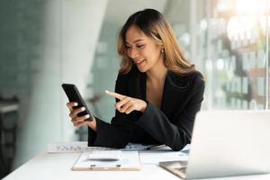 donna d'affari asiatica agitando i pugni, ha ricevuto buone notizie su smartphone mobile in ufficio, rete di social media, videochiamate, comunicazione. foto