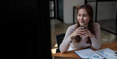 giovane donna asiatica d'affari in abbigliamento casual intelligente che discute di affari e sorride mentre si siede nel coworking creativo foto