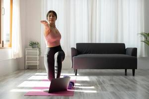 il giovane istruttore di fitness asiatico dà una lezione di video di yoga mostra l'esercizio di stretching prima della webcam del laptop in modalità conferenza. donne motivate partecipano ad allenamenti sportivi virtuali foto