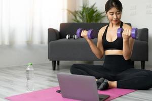 giovane donna asiatica che fa esercizi di fitness a casa attraverso la classe virtuale foto
