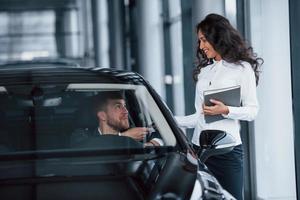 è tuo adesso. cliente maschio e donna d'affari moderna nel salone dell'automobile foto