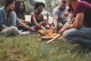 arrostire sulle fiamme del fuoco. un gruppo di persone fa un picnic sulla spiaggia. gli amici si divertono durante il fine settimana foto