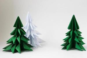 due alberi di natale verdi di origami e uno bianco su fondo bianco. foto