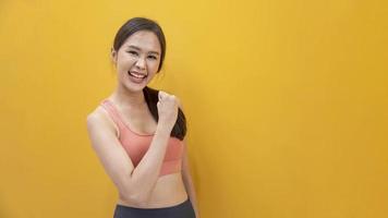 ritratto di donna atleta asiatica sana e magra in abbigliamento sportivo sorridente sullo sfondo giallo isolato per esercizio e allenamento foto