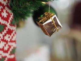 decorazioni natalizie albero verde appeso, confezione regalo dorata, avvolto attorno ad esso con un nastro dorato su sfondo bianco foto