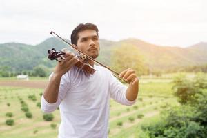 giovane musicista hipster che suona il violino nello stile di vita all'aperto della natura dietro la montagna. foto