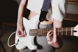 artista femminile che suona la chitarra elettrica eseguendo una canzone. vista ritagliata. donna con la chitarra bianca che prova a casa. musica come hobby e svago creativo. messa a fuoco selettiva foto