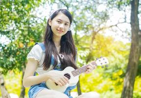 ragazza asiatica che suona l'ukulele e sorride felicemente nel parco. foto