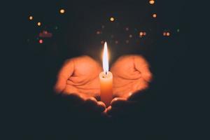 mani della donna che pregano alla luce delle candele foto