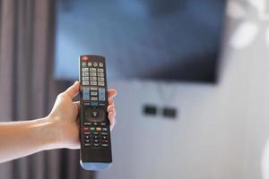 mano usando il telecomando per regolare la smart tv all'interno della stanza moderna a casa o in un hotel di lusso foto