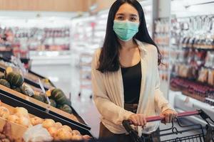 giovane donna che indossa la maschera protettiva per lo shopping nel supermercato. donna asiatica che indossa una maschera medica che fa la spesa nel negozio di alimentari durante la pandemia di coronavirus. crisi del coronavirus, focolaio di covid19. foto