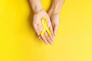 mano che tiene un nastro giallo su sfondo giallo per sostenere le persone che vivono e le malattie. giornata di prevenzione del suicidio di settembre, mese di sensibilizzazione sul cancro infantile e concetto di giornata mondiale del cancro foto