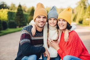 ritratto all'aperto di una bella donna bruna, un bell'uomo, una bella bambina che si abbraccia insieme, ha un umore piacevole, cammina nel parco, goditi un'atmosfera calma e uno splendido clima soleggiato. famiglia amichevole foto