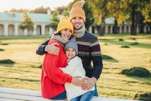 ritratto all'aperto di bella donna sorridente, bell'uomo e la loro piccola figlia carina stanno insieme contro l'antico bilduing nel parco, indossano abiti a maglia, fanno un'escursione interessante foto