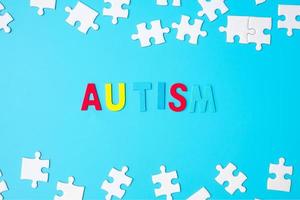 testo di autismo con pezzi di puzzle bianchi su sfondo blu. concetti di salute, disturbo dello spettro autistico e giornata mondiale di sensibilizzazione sull'autismo foto