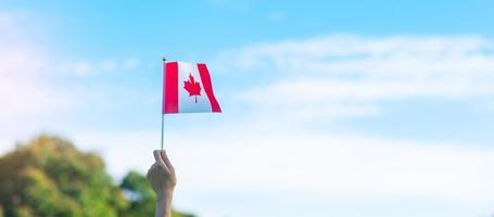mano che tiene la bandiera del Canada su sfondo blu cielo. canada giorno e concetti di celebrazione felice foto
