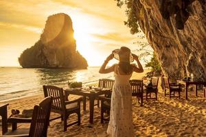 turista donna in abito bianco cena nella grotta del ristorante sulla spiaggia di phra nang al tramonto, railay, krabi, thailandia. concetto di vacanza, viaggio, estate, voglia di viaggiare e vacanza foto