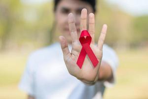 mano che tiene il nastro rosso per sostenere le persone che vivono e le malattie. concetto di assistenza sanitaria e sesso sicuro. dicembre giornata mondiale contro l'aids e mese di sensibilizzazione sul cancro del mieloma multiplo foto