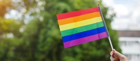 mani che mostrano la bandiera arcobaleno lgbtq su sfondo verde della natura. sostenere la comunità lesbica, gay, bisessuale, transgender e queer e il concetto di mese dell'orgoglio foto