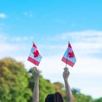 mano che tiene la bandiera del Canada su sfondo blu cielo. canada giorno e concetti di celebrazione felice foto