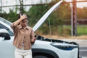 autista donna che utilizza il telefono cellulare durante l'auto problematica. guasto o macchina rotta sulla strada. concetto di assicurazione, manutenzione e servizio del veicolo foto