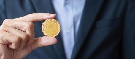 mano d'uomo d'affari che tiene criptovaluta dogecoin d'oro, la cripto è denaro digitale all'interno della rete blockchain, viene scambiata utilizzando la tecnologia e lo scambio online. concetto finanziario decentralizzato foto