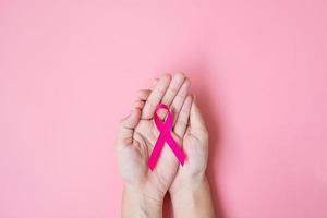 mese di sensibilizzazione sul cancro al seno di ottobre, mano di donna adulta che tiene nastro rosa su sfondo rosa per sostenere le persone che vivono e le malattie. concetto internazionale delle donne, della madre e della giornata mondiale del cancro foto