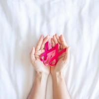 mese di sensibilizzazione sul cancro al seno di ottobre, mano di donna adulta che tiene nastro rosa su sfondo rosa per sostenere le persone che vivono e le malattie. concetto internazionale delle donne, della madre e della giornata mondiale del cancro foto