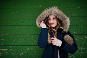bella ragazza bruna in abiti caldi invernali. modello su giacca invernale su sfondo di legno verde. foto