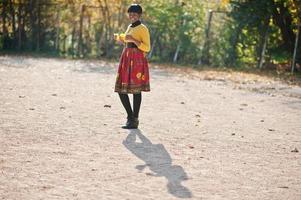 ragazza afroamericana in abito giallo e rosso al parco autunnale dorato. foto
