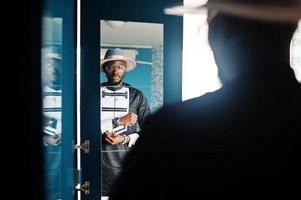 ricco uomo africano che guarda lo specchio sull'armadio del suo appartamento. ritratto di uomo di colore di successo indoor. foto