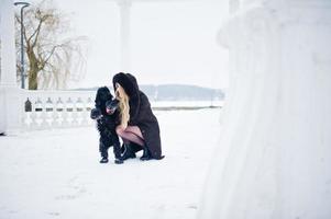 eleganza ragazza bionda in pelliccia abbraccia un piccolo cane nero al giorno d'inverno. foto