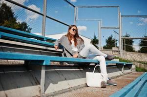 ragazza in cappotto grigio con occhiali da sole al piccolo stadio di strada. foto