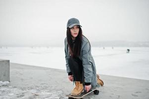 elegante ragazza bruna con berretto grigio, casual street style con skateboard in giornata invernale. foto