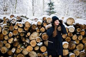 bella ragazza bruna in abiti caldi invernali. modello su giacca invernale e cappello vicino a ceppi di alberi. foto