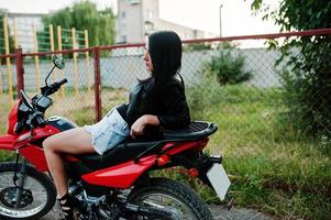 ritratto di una donna fresca e fantastica in abito e giacca di pelle nera seduta su una bella moto rossa. foto