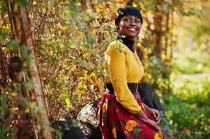 ragazza afroamericana in abito giallo e rosso al parco autunnale dorato. foto