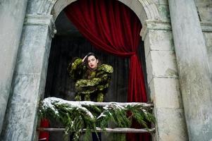 ragazza bruna in pelliccia verde contro il vecchio arco con colonne e tende rosse. foto