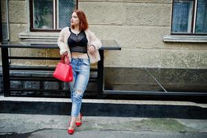 ragazza dai capelli rossi con borsa rossa poste in strada della città. foto