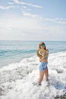 bellissima modella che si rilassa su una spiaggia di mare, indossa jeans corti, camicia leopardata e cappello. foto