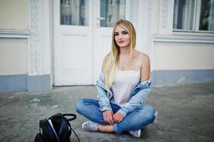 ragazza bionda indossare su jeans con zaino poste contro la vecchia porta. foto